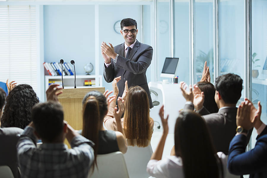 A speaker being applauded by a group of professionals